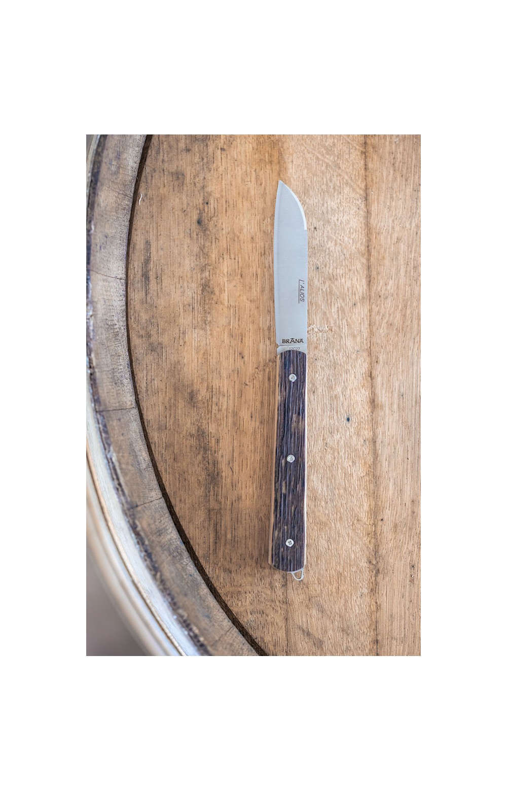 Photo couteau Alios en douelle de whisky tourbé français (chêne de barrique ) en position ouverte sur un tonneau